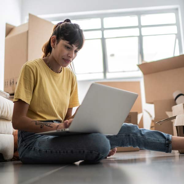 A woman sitting on the floor with a laptop, exploring condo insurance policies in Grand Junction, CO
