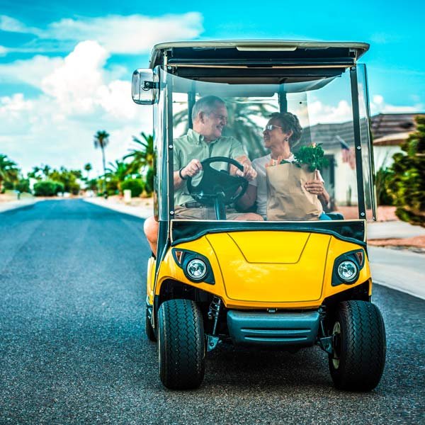 An elderly couple driving a golf cart insured by Ideal Insurance Agency in the Grand Junction area