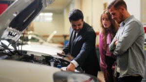 Three people are inspecting a car engine in Grand Junction, CO, discussing car insurance plans
